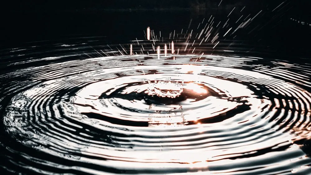 Una gota cayendo sobre agua oscura y las ondas que abre