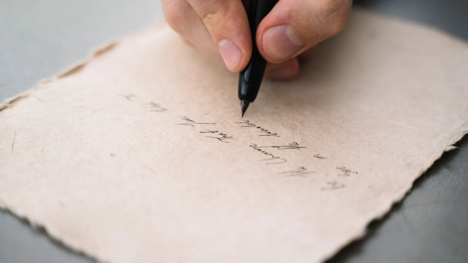Una mano escribiendo una carta a mano sobre papel, en un fondo oscuro