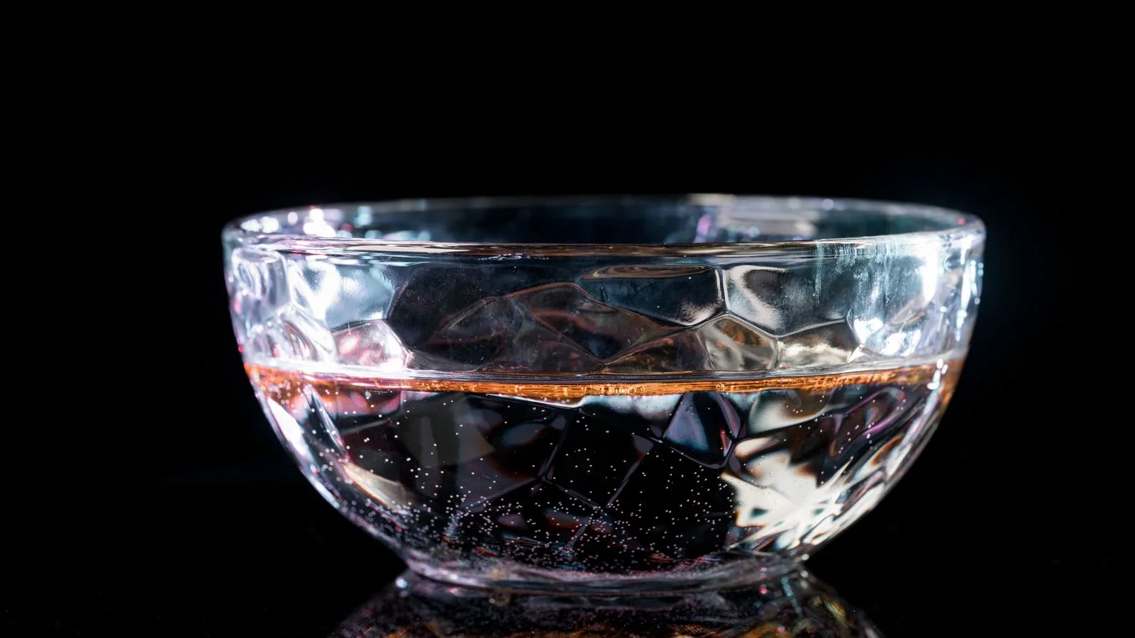 Un cuenco de cristal con agua sobre fondo negro, con la luz deformada al atravesarlo