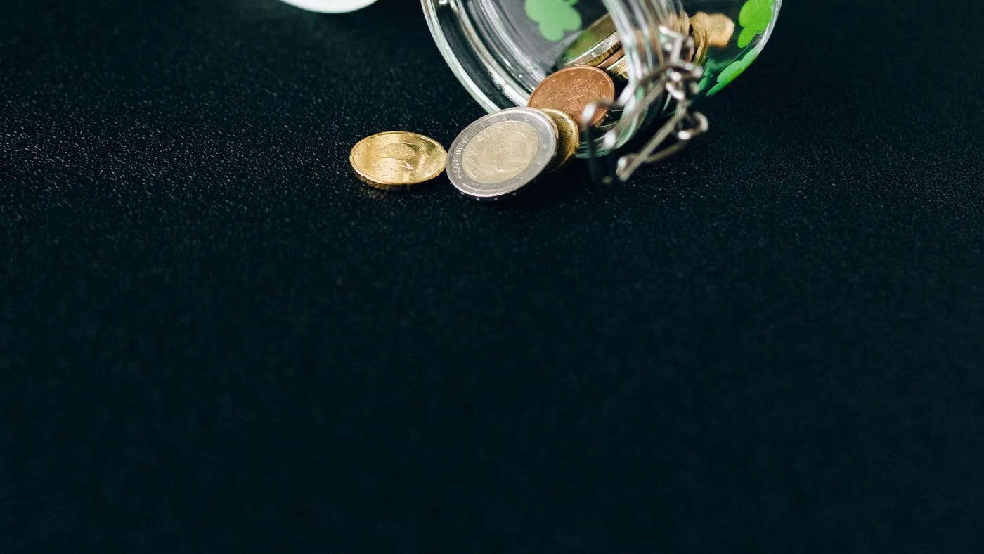 Un frasco de vidrio volcado con monedas sobre fondo oscuro