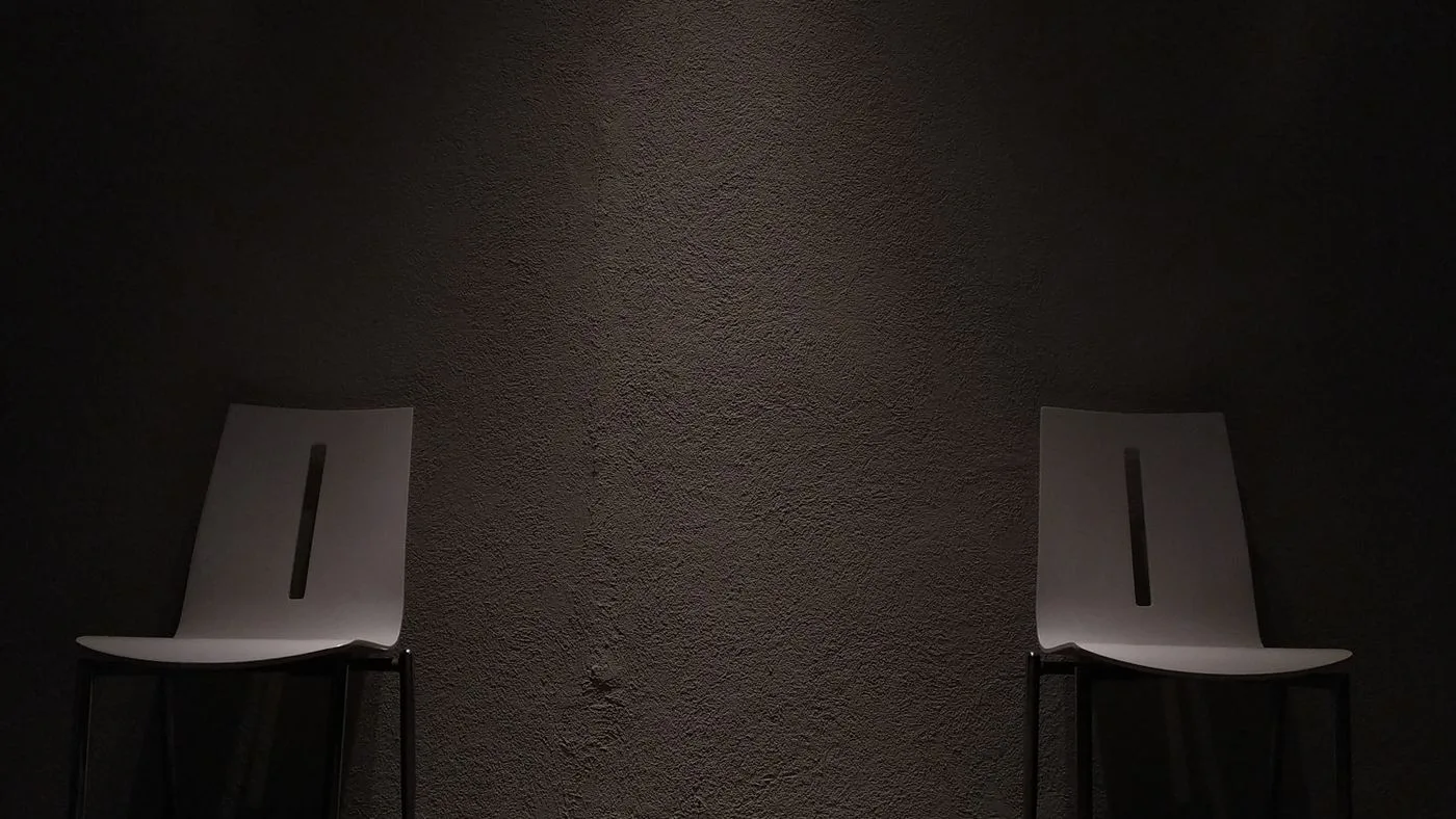 Dos sillas vacías separadas contra una pared oscura, como en una sala de espera