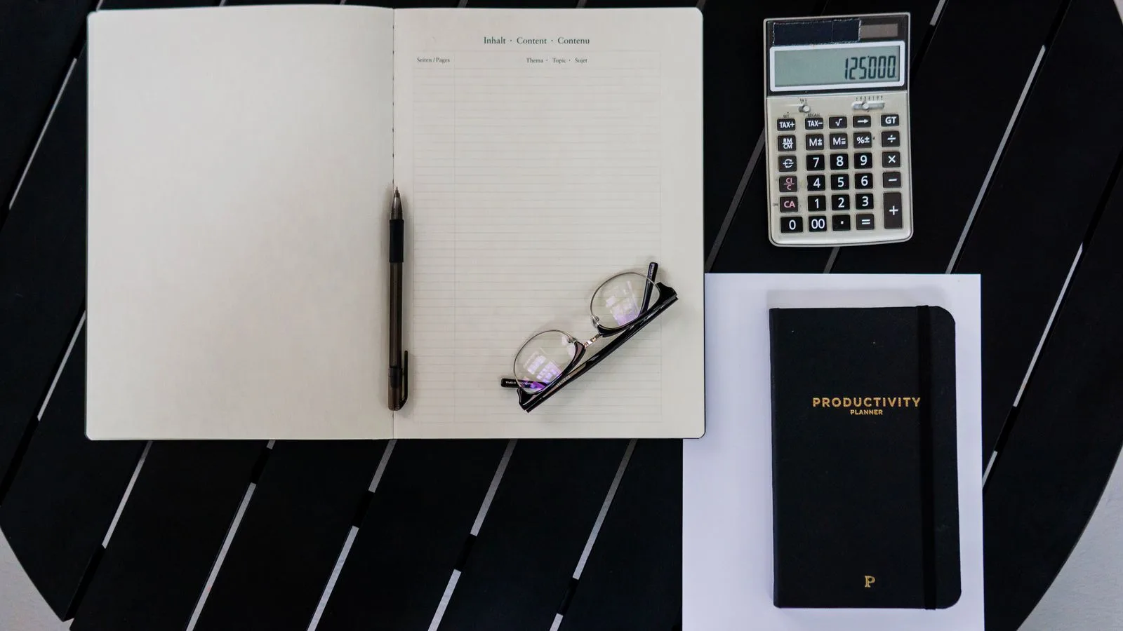 Un cuaderno, una calculadora y una pluma sobre una superficie negra