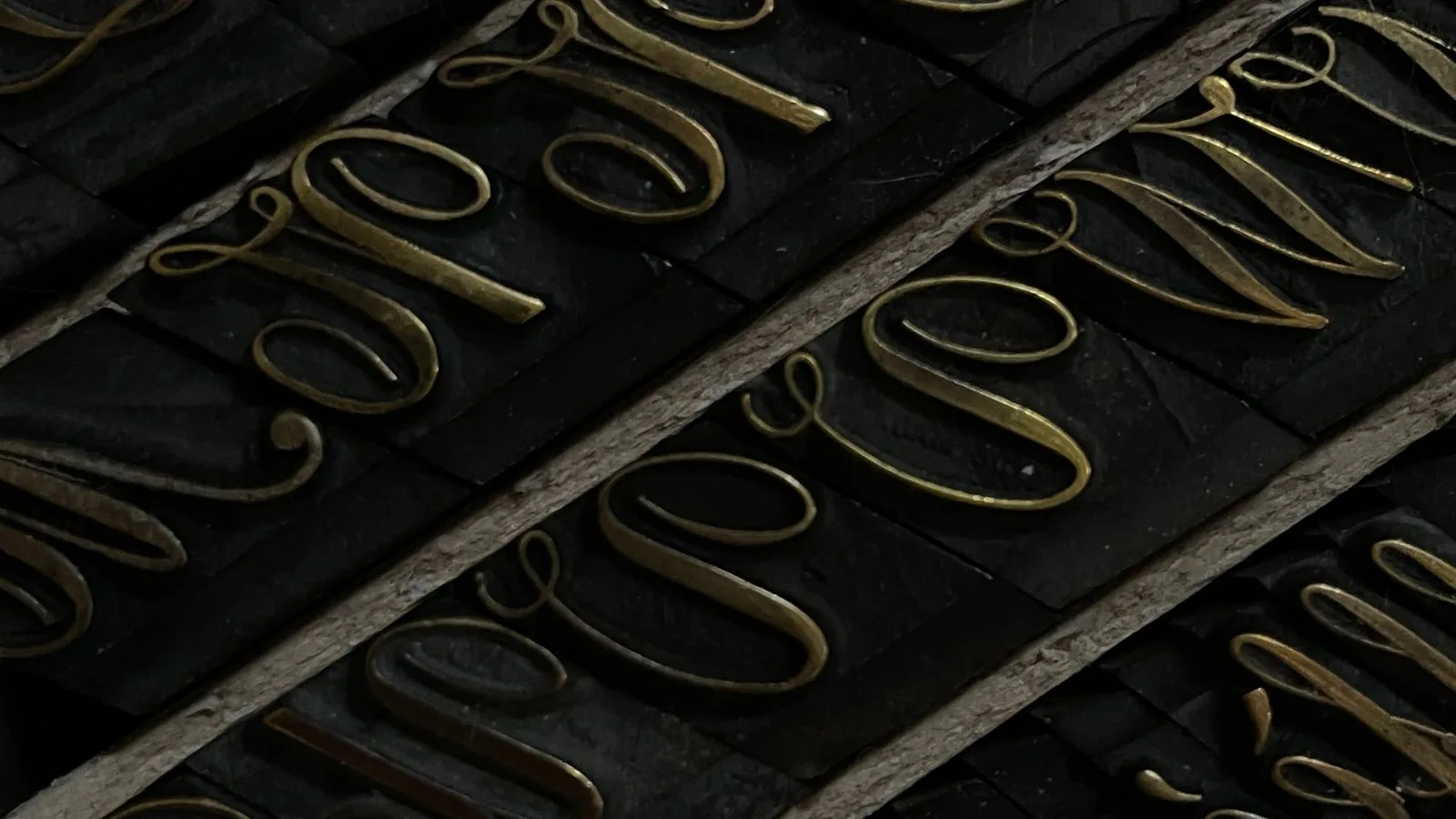 Tipos de imprenta de bronce alineados en filas sobre fondo negro