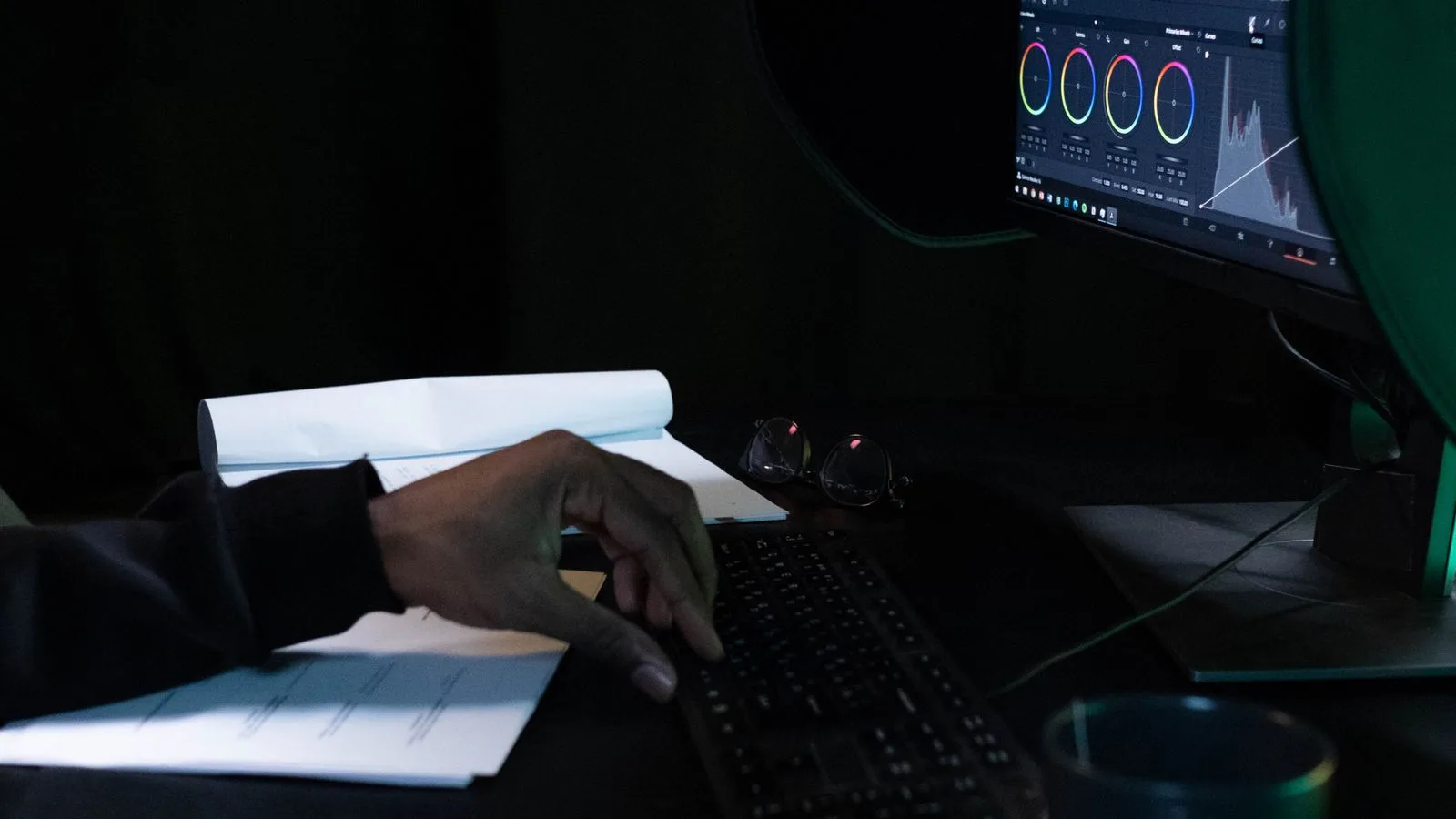 Una mano editando video ante un monitor en una habitacion a oscuras