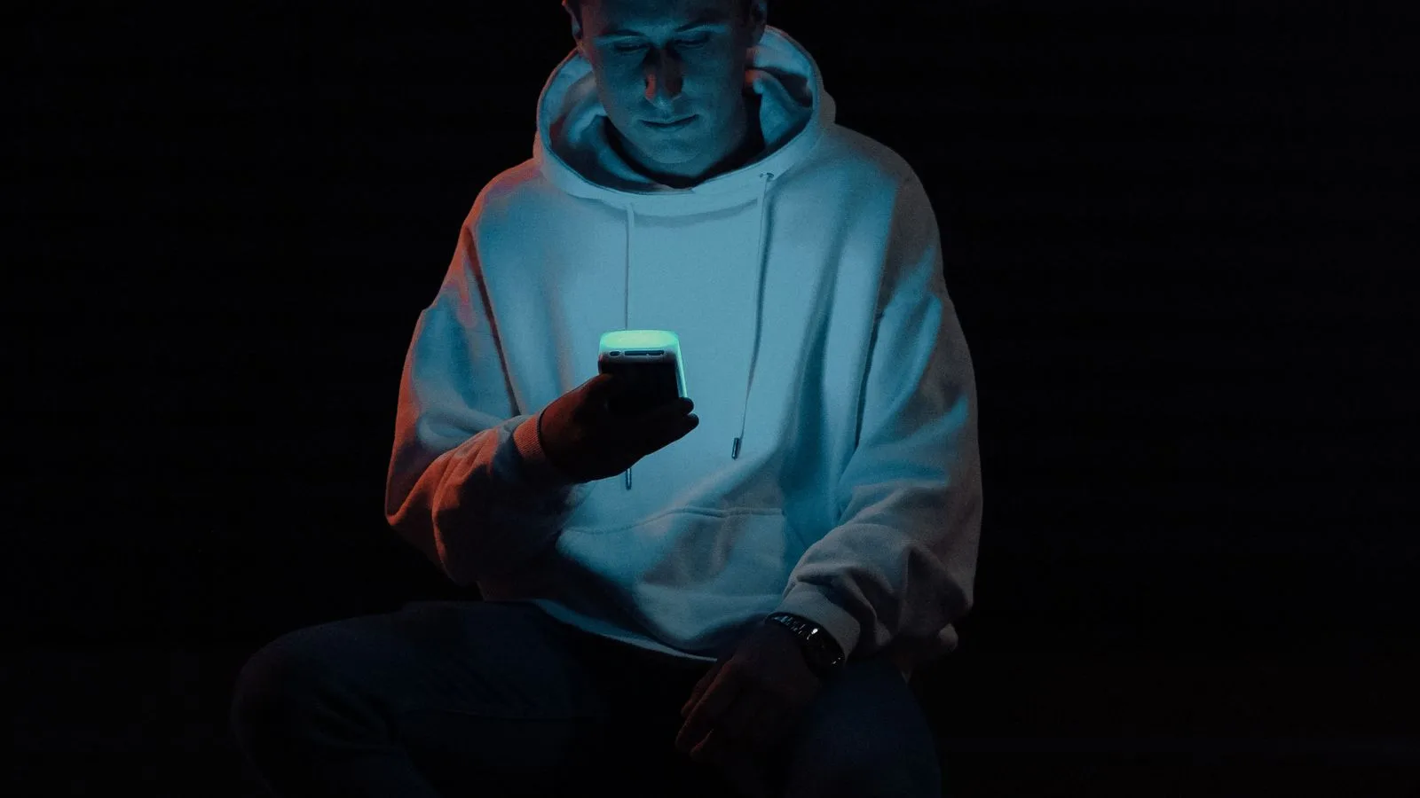 Una persona con capucha, a oscuras, con la cara iluminada por la pantalla del teléfono