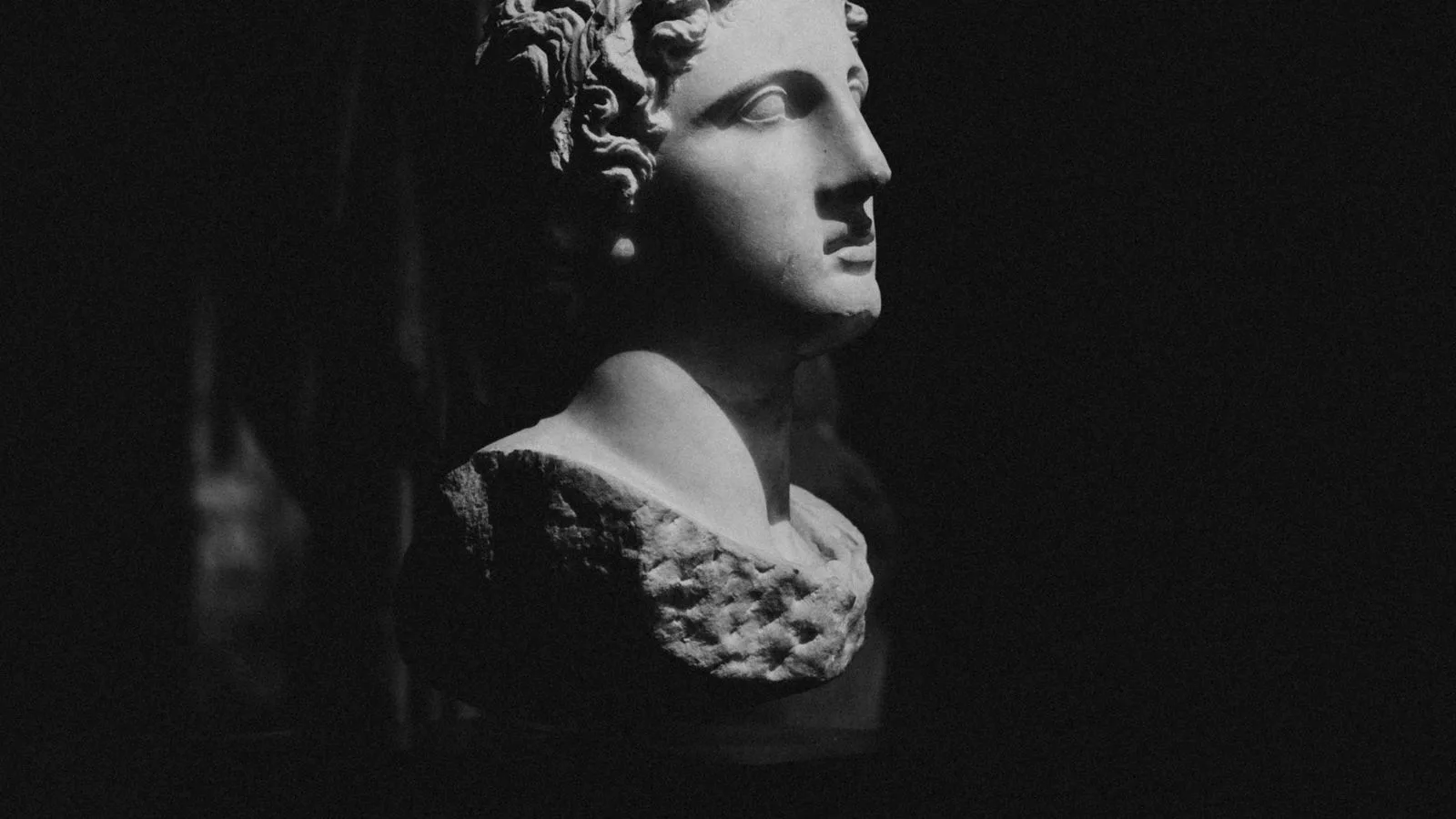 Un busto de mármol clásico iluminado sobre fondo negro