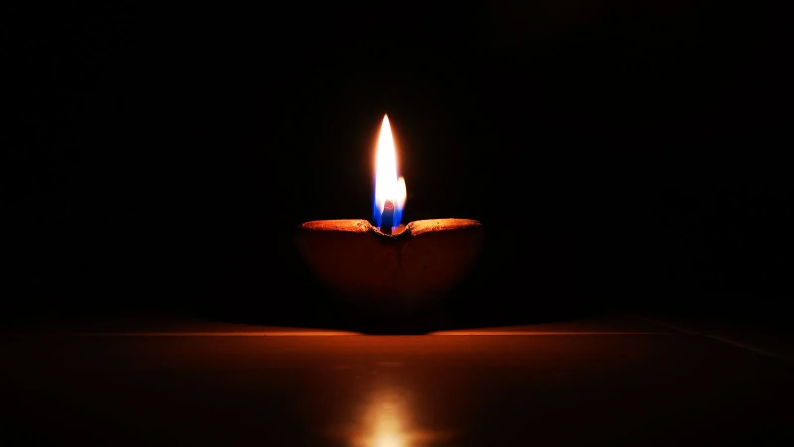Una lámpara de barro encendida en la oscuridad, con su reflejo en la mesa