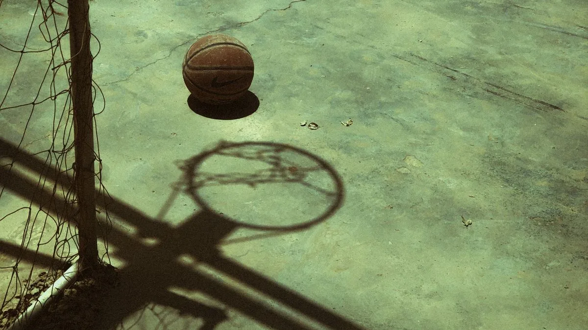 Un balón de baloncesto sobre la cancha, con la sombra del aro proyectada en el suelo