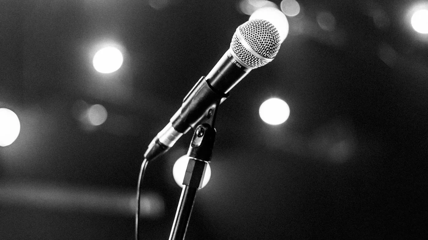 Un micrófono en un escenario vacío, iluminado por un foco, en blanco y negro