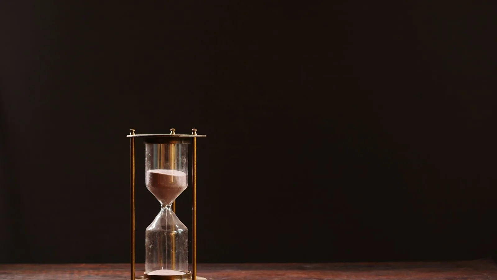 Un reloj de arena de latón sobre una mesa de madera, contra un fondo casi negro