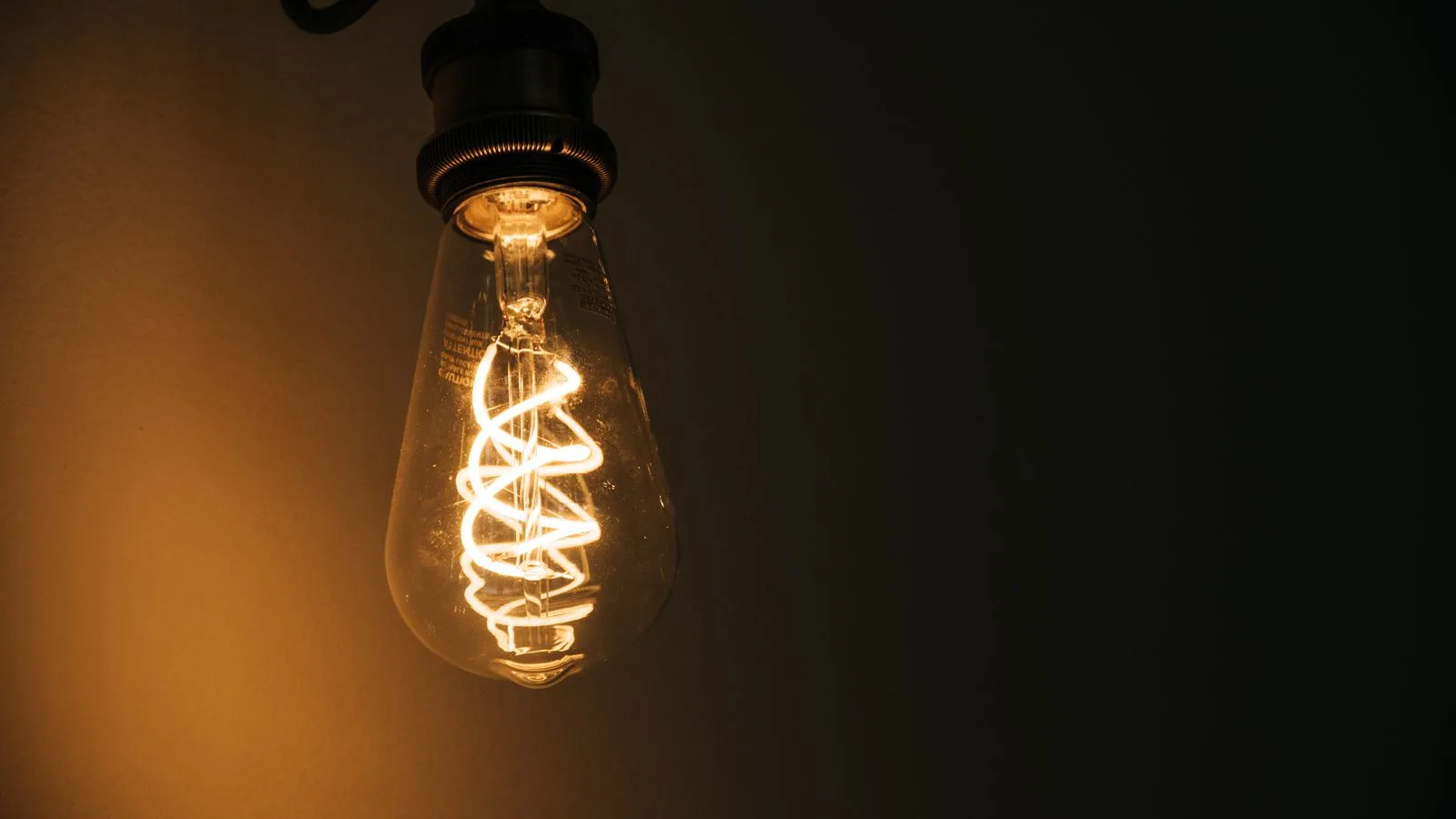 Una bombilla incandescente de filamento encendida sobre fondo oscuro