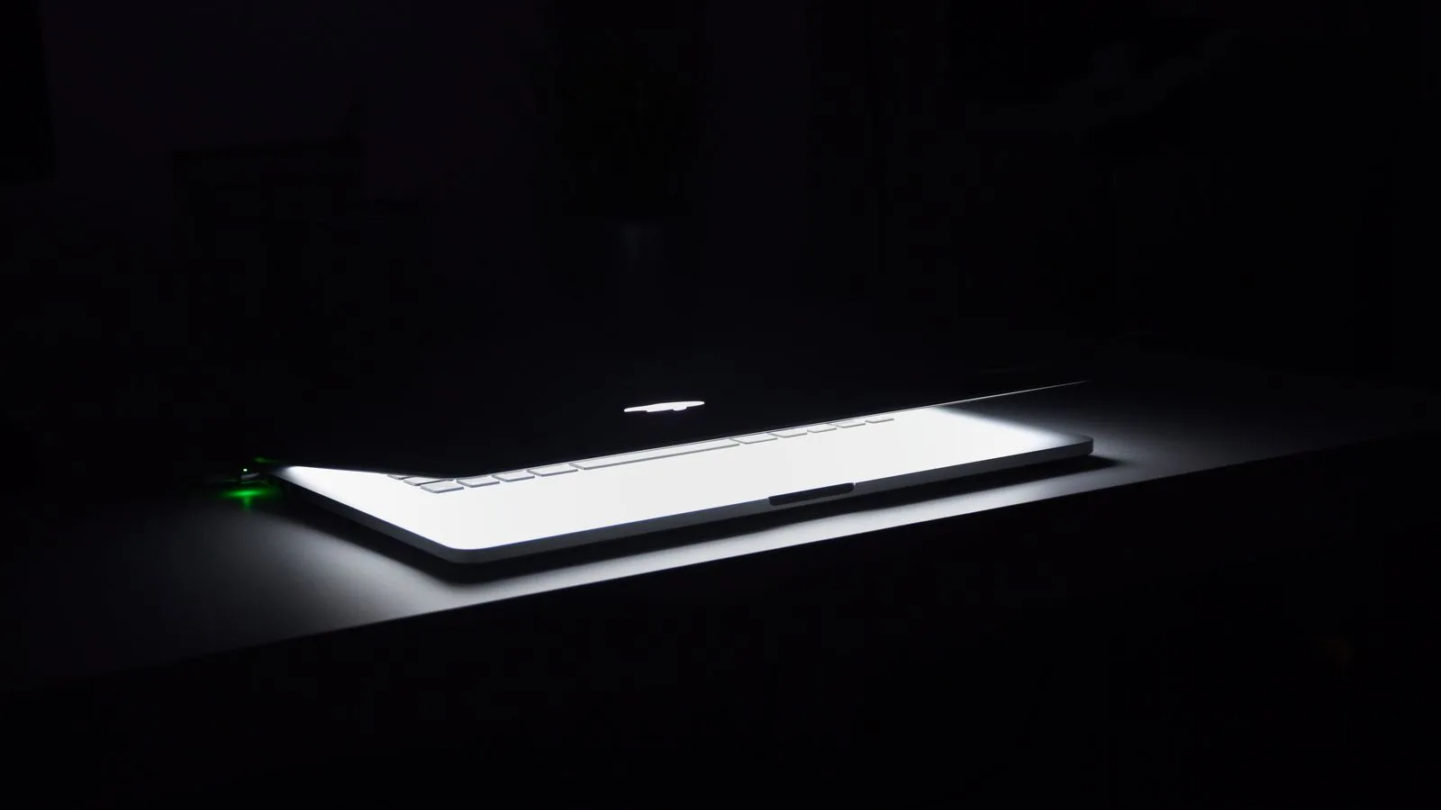 Una laptop entreabierta con el teclado encendido sobre un escritorio a oscuras