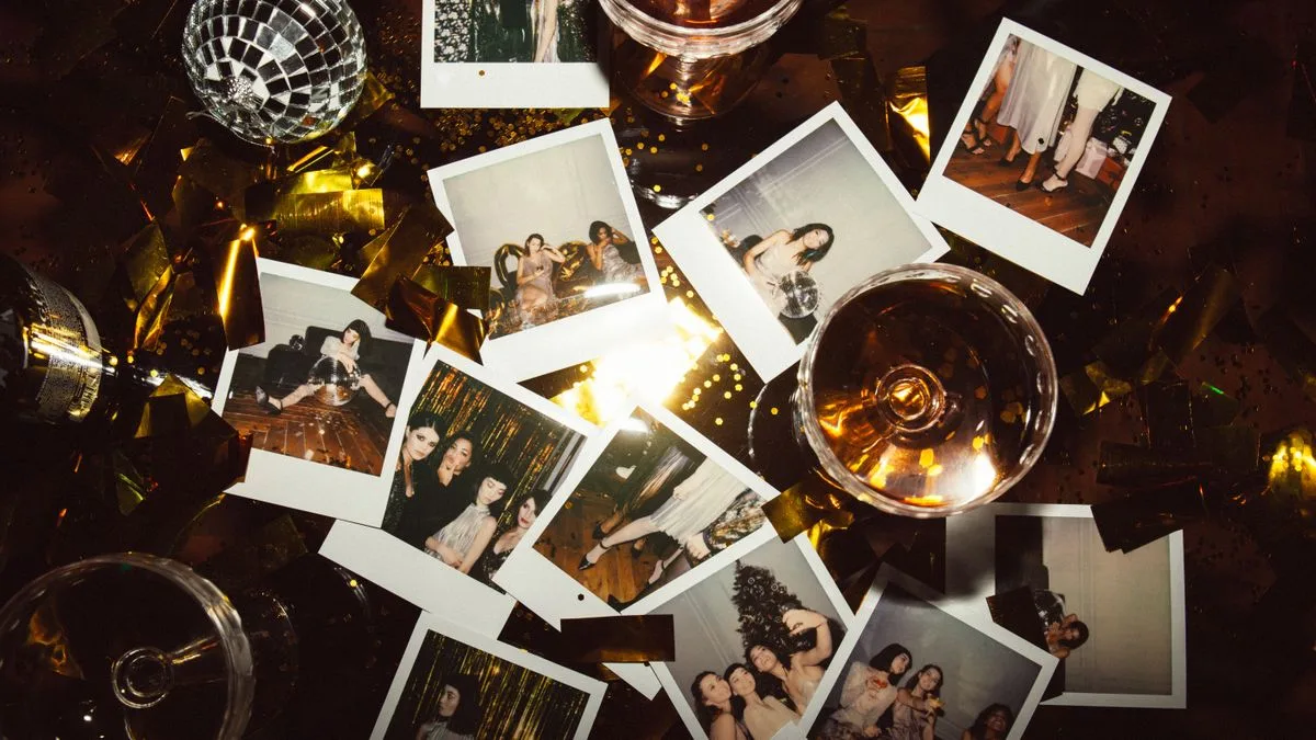 Fotos instantáneas esparcidas entre copas, luces y una bola disco, en una mesa de fiesta