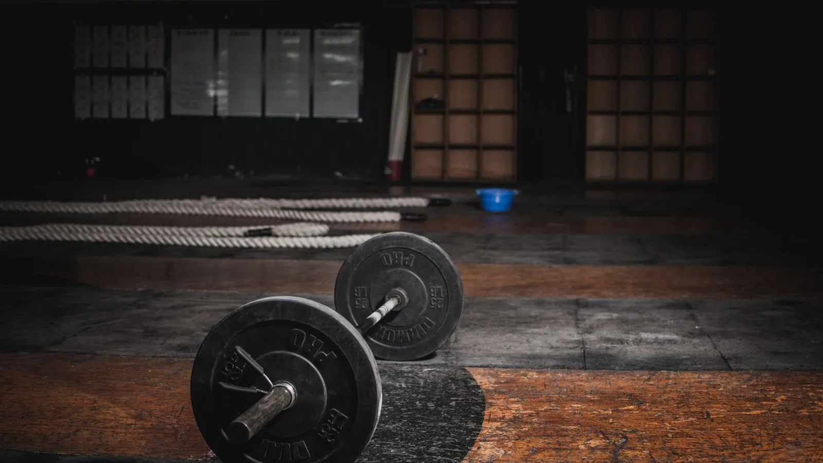 Una barra de gimnasio sola en el suelo de un gimnasio en penumbra
