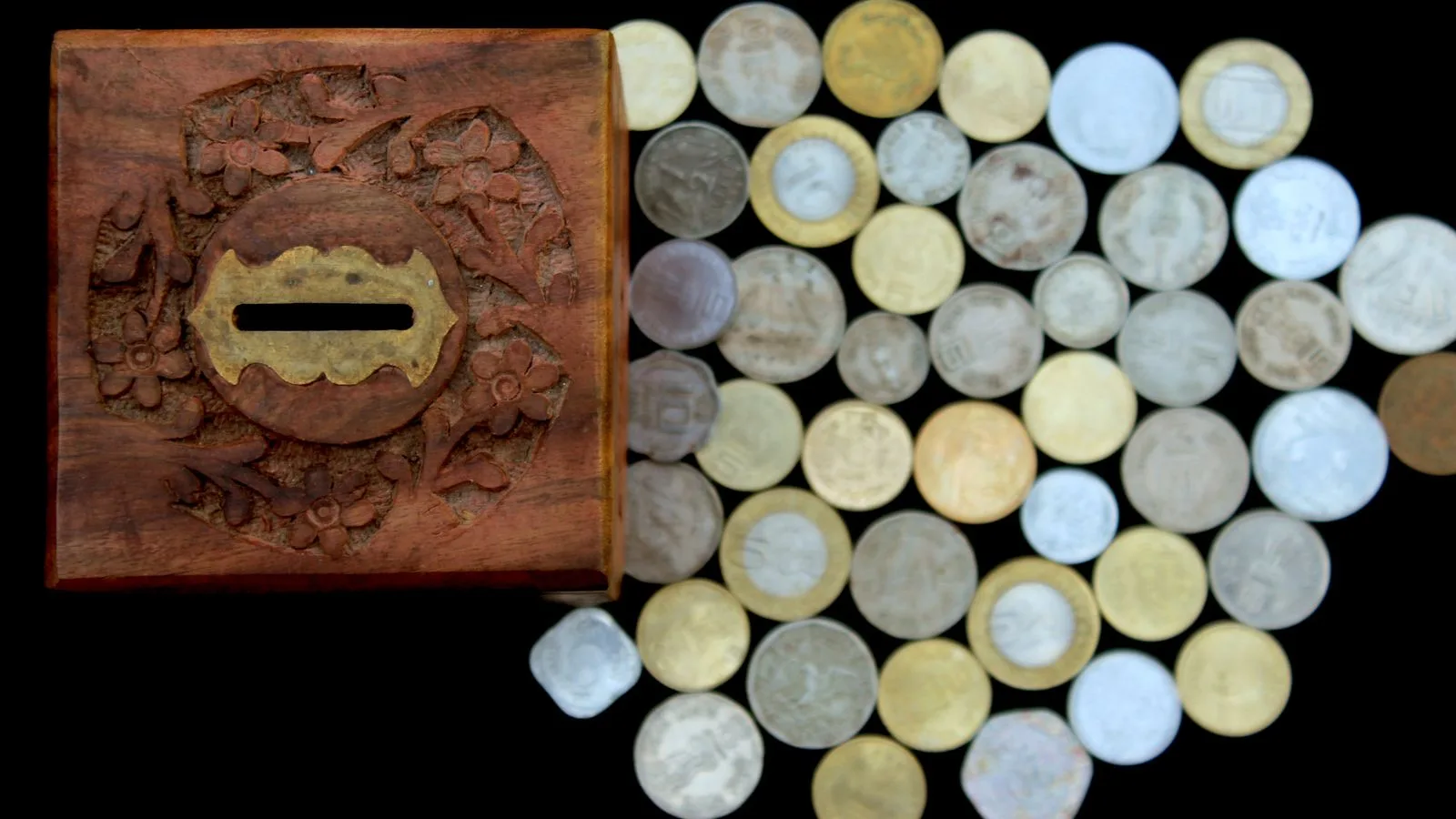 Una alcancía de madera y monedas sueltas sobre una superficie negra