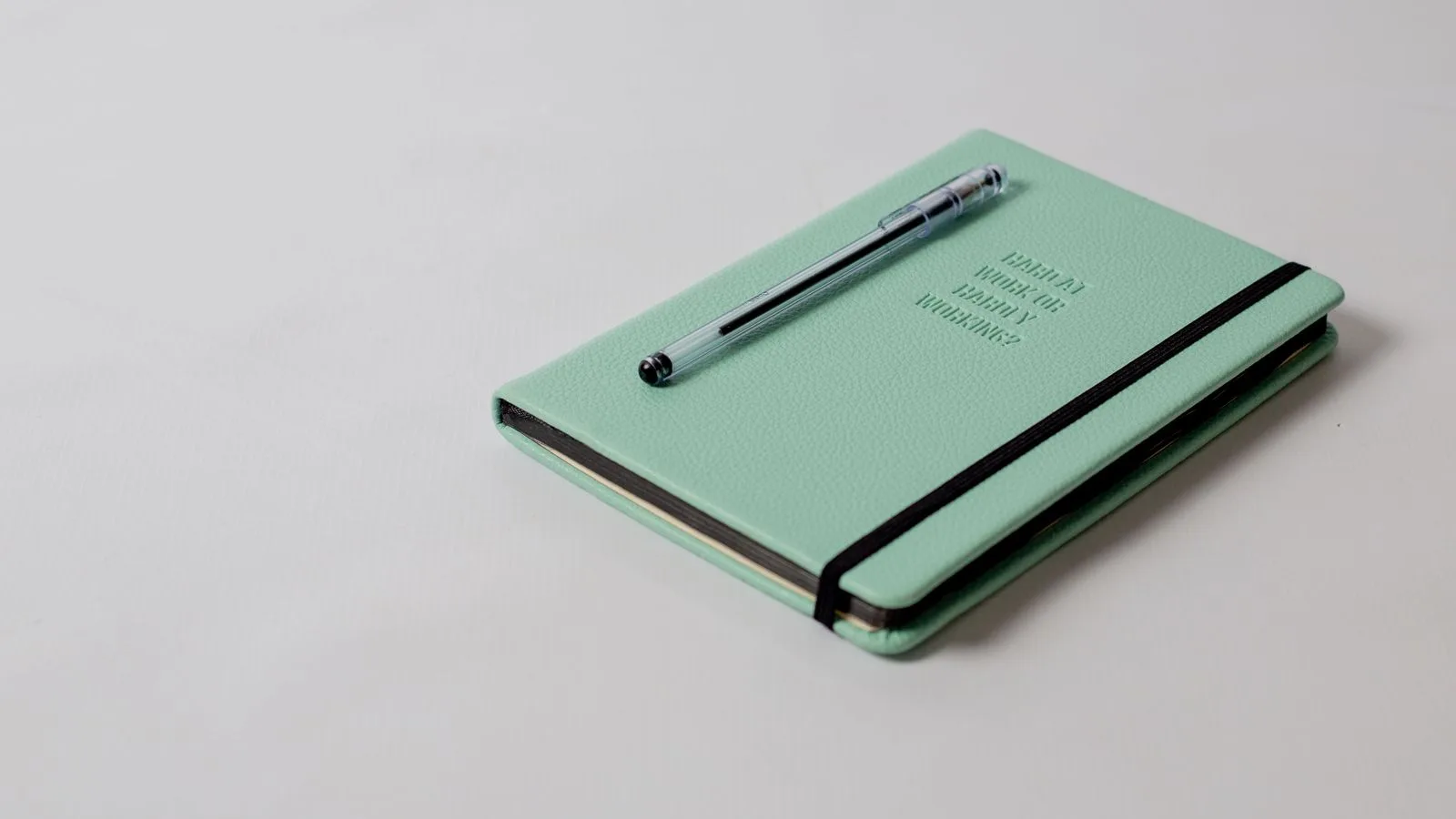 Una libreta verde menta cerrada con un bolígrafo encima, lista para la revisión semanal