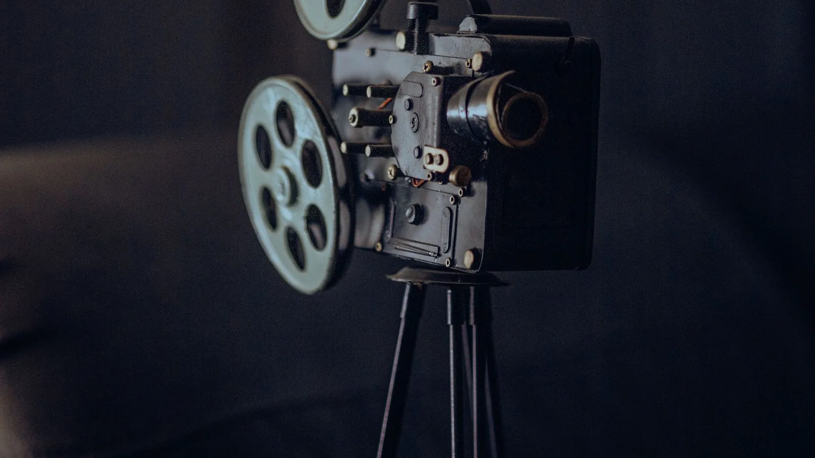 Un proyector de cine antiguo sobre su trípode, contra un fondo oscuro