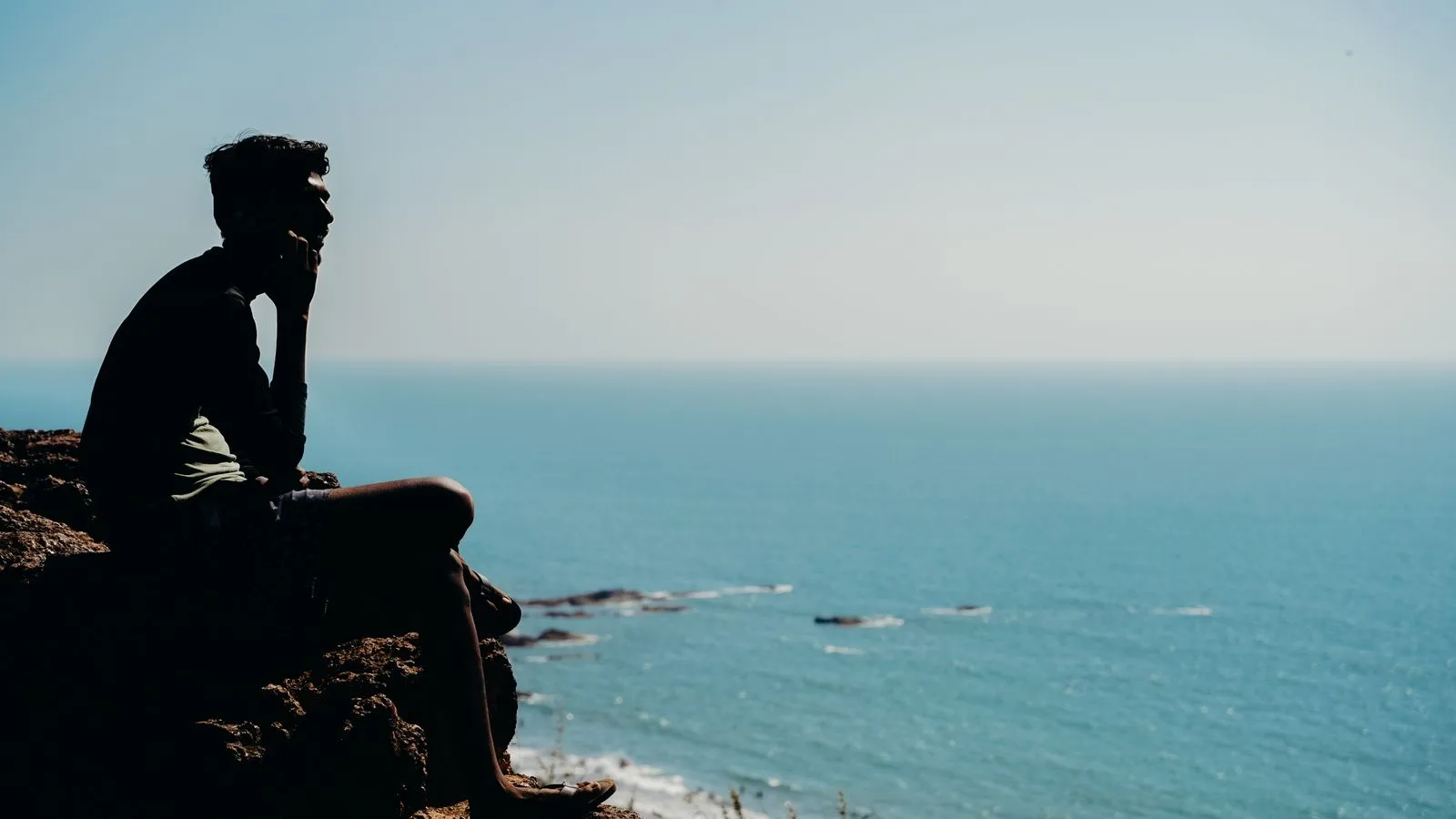 La silueta de una persona de pie sobre las rocas, mirando el mar al atardecer