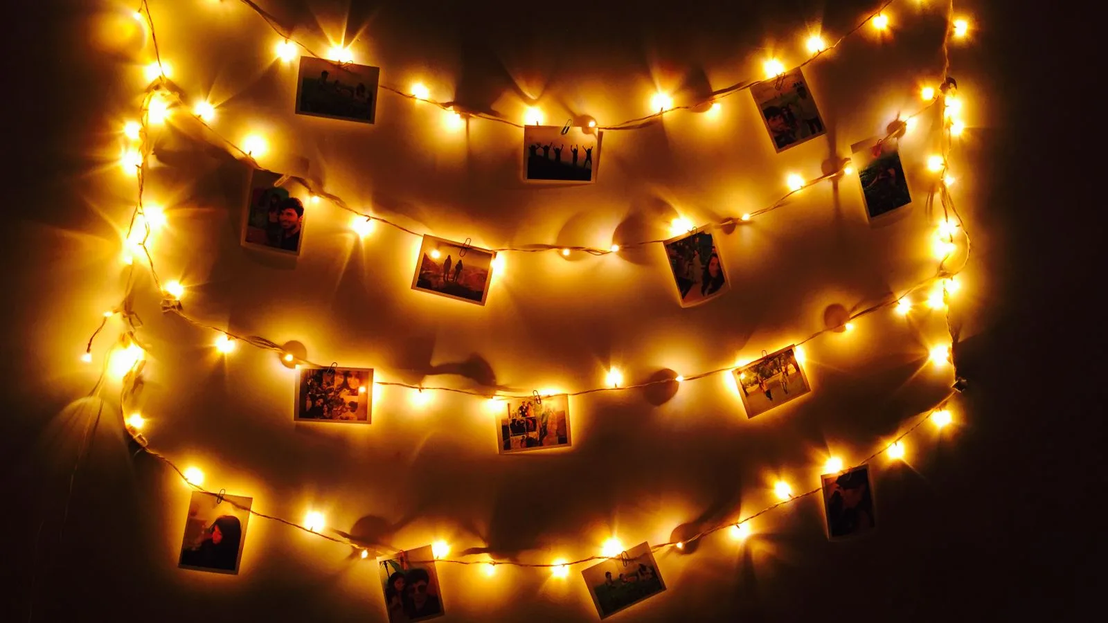 Fotos pequeñas colgadas con pinzas de una guirnalda de luces sobre una pared oscura